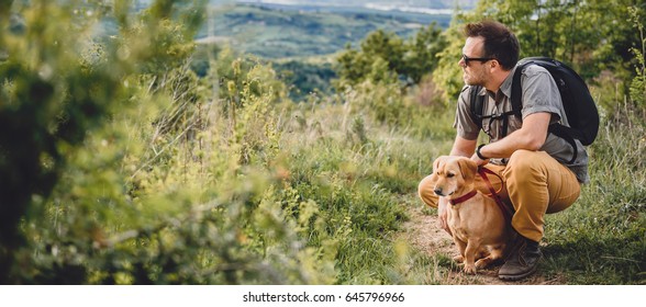 Man Wearing Sunglasses With A Small Yellow Dog Resting At The Hiking Trail