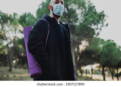 Man wearing a surgical mask holding a purple yoga mat in a park. Exercise in nature outdoors concept - Powered by Shutterstock