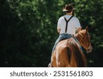 Man wearing suspenders and cowboy hat riding a horse outdoors in a rural setting with green trees in the background.