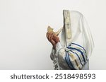 Man wearing a tallit, traditional Jewish prayer shawl with blue stripes and Hebrew text, blowing into a shofar, rams horn used in Jewish ceremonies, Rosh Hashanah. Elements of Jew religious tradition