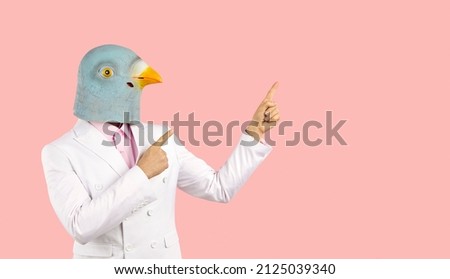 Man wearing trendy white suit and funny pigeon bird mask standing isolated on solid pastel pink colour background and pointing both index fingers at blank marketing text copyspace on right side