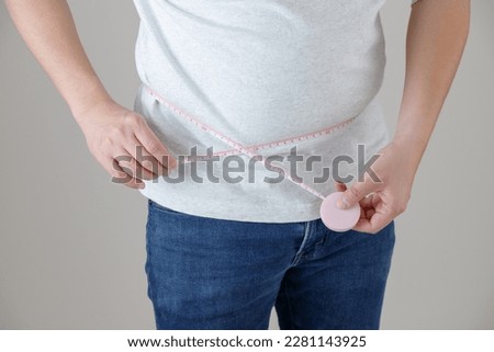 A man wearing a T-shirt and jeans is measuring his waist size, implying an image of health management and dieting.