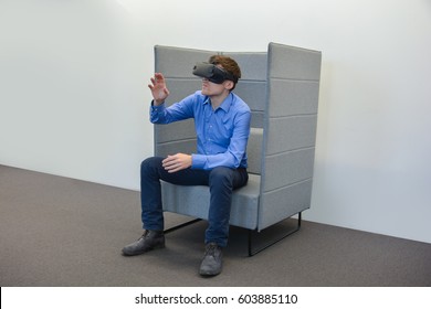 Mann mit Virtual-Reality-Gerät. Seitenansicht, lächelnder Gesichtsausdruck, sitzend im Sessel mit einer Hand erhöht. Business casual style New Virtual Device 2017.