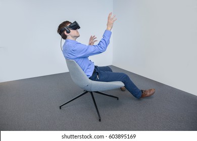 Man wearing virtual reality device. Side close view, smiling face expression, sitting in the armchair with  hands raised, touching. Business casual style. New Virtual  device 2017.