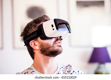 Man wearing virtual reality goggles, sitting in living room