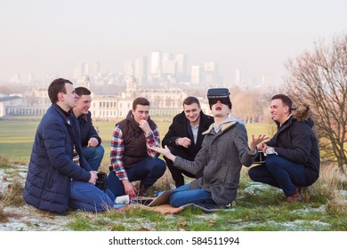 Man Wearing Virtual Reality Goggles. Group Of People Sitting In Park