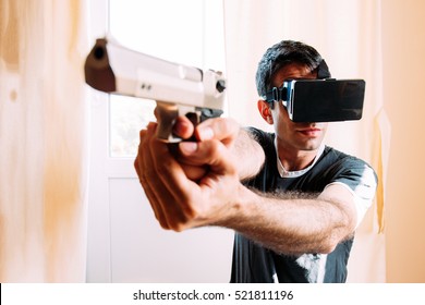 Man wearing VR goggles and holding a handgun pistol - playing a virtual reality game at home