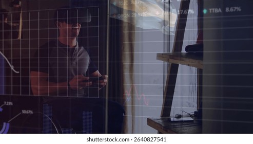 Man wearing VR headset and holding controllers exploring virtual financial charts in home office. Technology, innovation, digital, immersive, analytics, modern, workspace