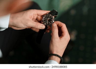 A man is wearing a watch and is adjusting it. The watch is black and gold - Powered by Shutterstock