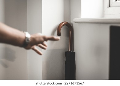 A man wearing a watch reaching for an umbrella, ready to go outside - Powered by Shutterstock