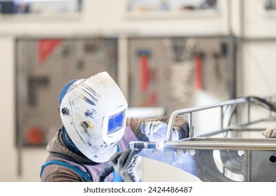 a man wearing a welding helmet is welding a piece of metal in a factory - Powered by Shutterstock