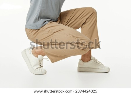 man wearing white sneakers and casual beige pants squatting on studio background. side view