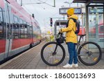 A man, wearing winter clothes, at the station, is about to get on the train, with his bicycle.