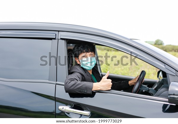 A man\
wearing a work suit drives a sedan to work in the city. wearing a\
medical mask to prevent infection during the coronavirus epidemic\
The driver of the sedan wears a mask for\
Covid-19.