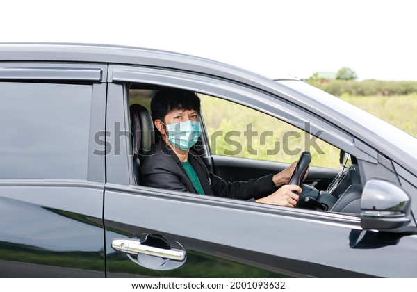 A man\
wearing a work suit drives a sedan to work in the city. wearing a\
medical mask to prevent infection during the coronavirus epidemic\
The driver of the sedan wears a mask for\
Covid-19.