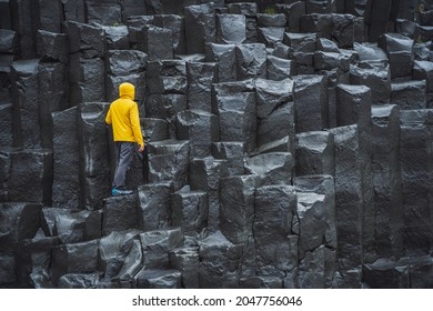 Man wearing yellow coat looking up at Reynisdrangar basalt columns at Reynisfjara Beach, Iceland - Shutterstock ID 2047756046