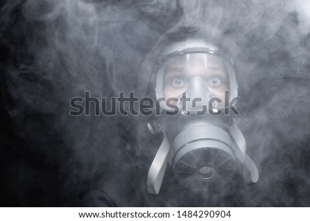 Man wears a gasmask in a smokey, toxic atmosphere. 