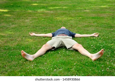 Man wears grey t-shirt, khaki short comfortable lying down by stretching his arms and legs on lawn in the park