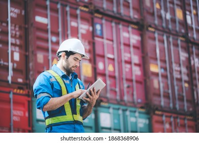 Man wears hardhat and reflection shirt and checking tablet with blurry metal containers in background. Concept of inventory and logistic management. - Powered by Shutterstock