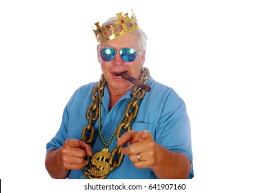 A man wears a King Crown, Gold Chains, Sunglasses and smokes a Big Cigar. Isolated on white. Room for text. 