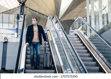 Man wears medical face mask, poses on escalator in airport, arrives from abroad, holds mobile phone and suitcase, protects from pandemic disease. Threat of epidemic in 2020, dangerous traveling - Powered by Shutterstock