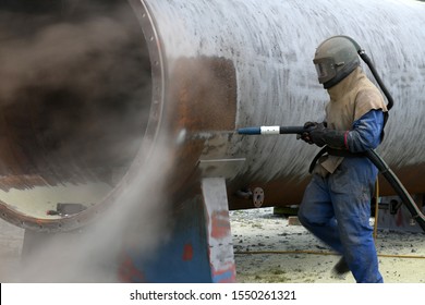 A man weating full safety gear uses ground glass to sandblast the steel casing of a meat drying machine for a rendering plant