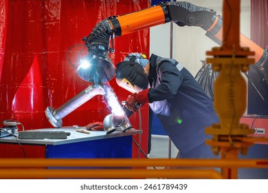 Man welder at work. Production of steel pipes. Welder works in factory. Welding machine in hands of man. Equipment for smoke extraction in production. Welder in mask protecting his face - Powered by Shutterstock