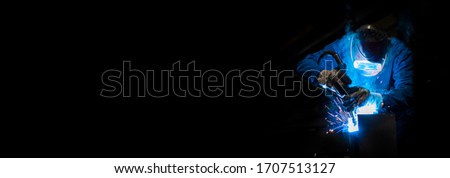 Man welding in a fabric with sparks, dark background