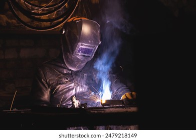 man in a welding mask welds a pipe in a dark workshop. welding smoke in the face, close-up - Powered by Shutterstock