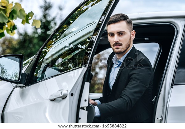 Man\
in a well tailored suit jacket next to a luxury\
car