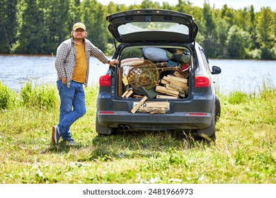 man went on a picnic stands next to an open trunk of a car with a bunch of stuff in it - Powered by Shutterstock