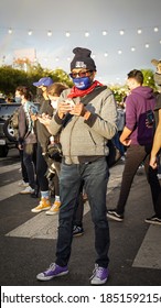 Man West Hollywood California 2020 after election day celebrating Joe Biden & Kamala Harris winning the White House. Wearing a Biden Harris mask & Lincoln project beanie on his phone on the crosswalk￼