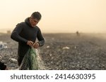 Man in wetsuit collecting fish from a net on the beach