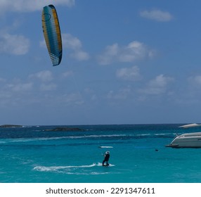 A man in a wetsuit kitesurfing in the light blue ocean water on a sunny day