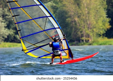 A man in wetsuit windsurfing on a river with forest background - Powered by Shutterstock