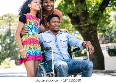 Man In A Wheelchair Enjoying A Walk Outdoors With Family.