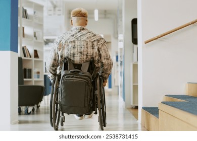 Man in wheelchair navigating through modern office hallway with backpack. White walls and carpeted stairs create an accessible environment - Powered by Shutterstock