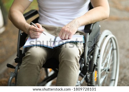 Man in wheelchair sits and holds notebook and pen. Learning professions of people with disabilities concept