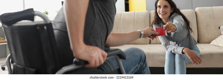 Man in wheelchair take condom from smiling wife sit on sofa, happy couple celebrate potency - Shutterstock ID 2219413169