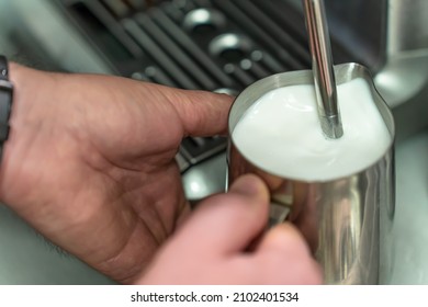 A man whisks milk for a latte in a steel jug.