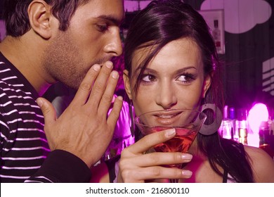 Man Whispering Into A Young Woman's Ear In A Bar