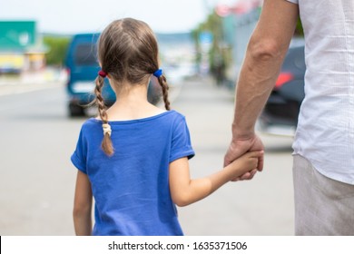 A man in white clothes leads a little girl by the hand along the street