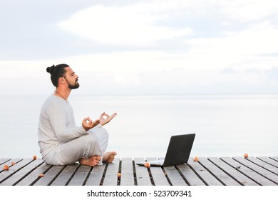 Man In White Clothes Meditating Yoga With Laptop On Wooden Pier