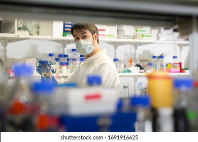 man with white coat and mouth protection standing behind a rack with chemicals