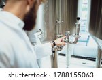 A man in a white coat stands in a beer factory and examines the quality of beer