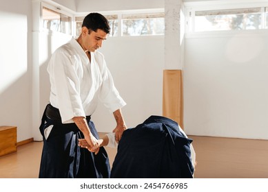 A man in a white gi and black hakama pants is demonstrating arm joint control on a partner, showcasing his black belt martial arts skills. - Powered by Shutterstock