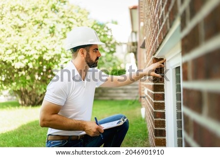 A man with a white hard hat holding a clipboard, inspect house