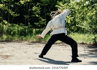 A man in a white kimono practices martial arts in a park - Powered by Shutterstock