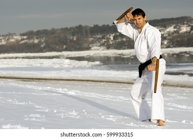 The Man In White Kimono Is Practicing Japanese Martial Arts With Tonfa In The Snow On Winter Background.