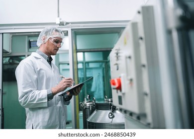 A man in a white lab coat is writing on a clipboard in front of a machine. Concept of professionalism and focus as the man takes notes while working in a laboratory setting - Powered by Shutterstock